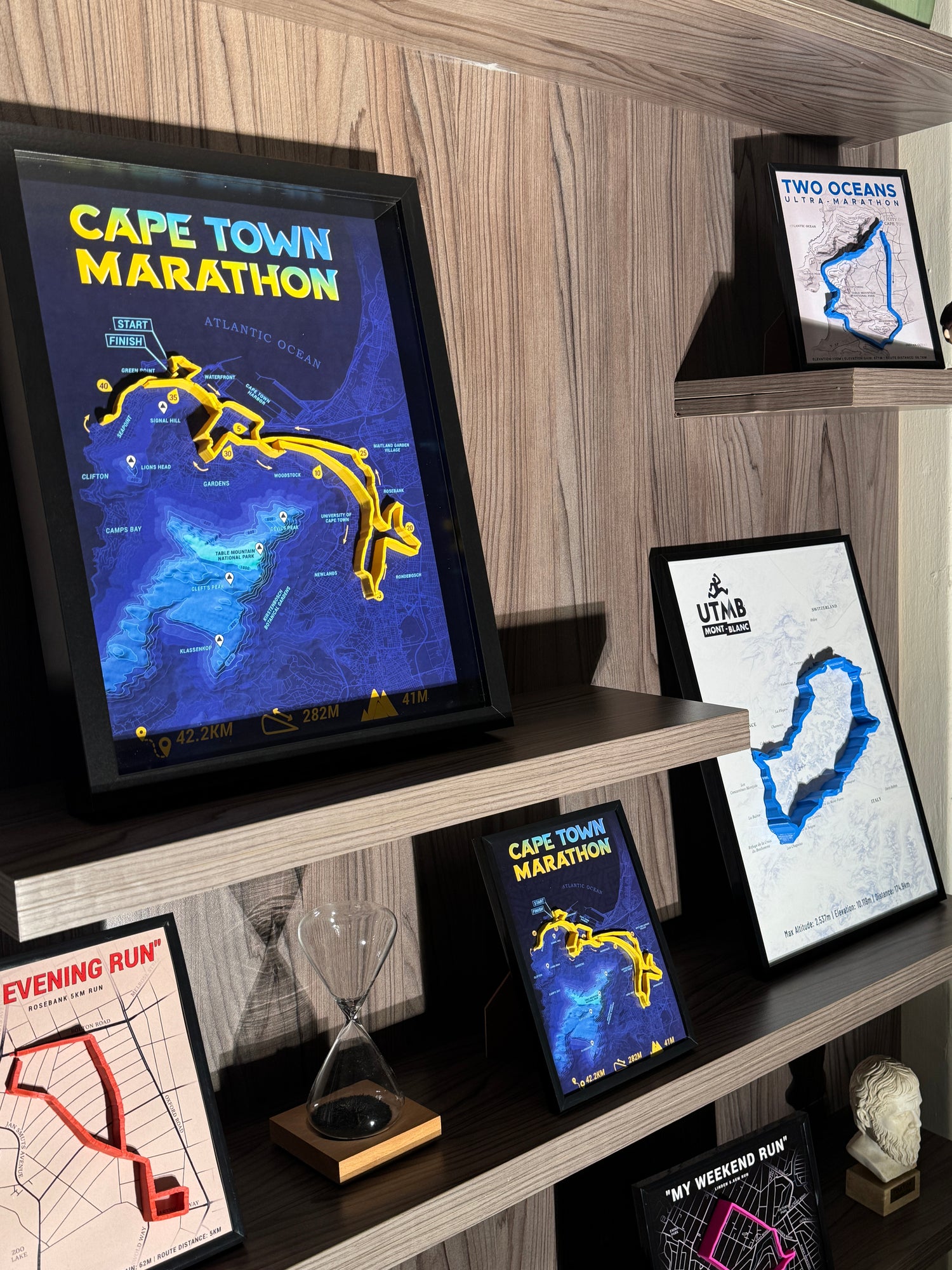 Framed maps of the Cape Town Marathon and other races on a wooden shelf.